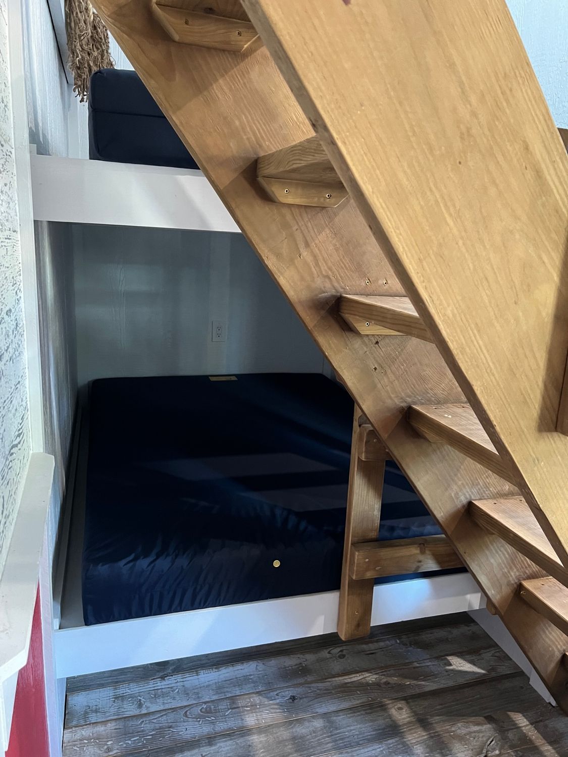 Wooden bunk beds with a built-in staircase. The lower bed is visible, and the upper bed is partially obscured.