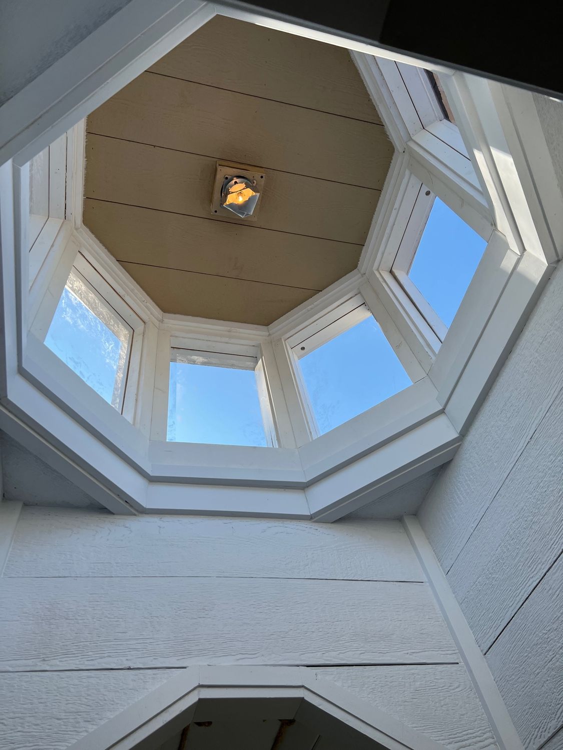 Looking up at a white octagonal skylight with blue sky visible through the windows, lit by a central light.