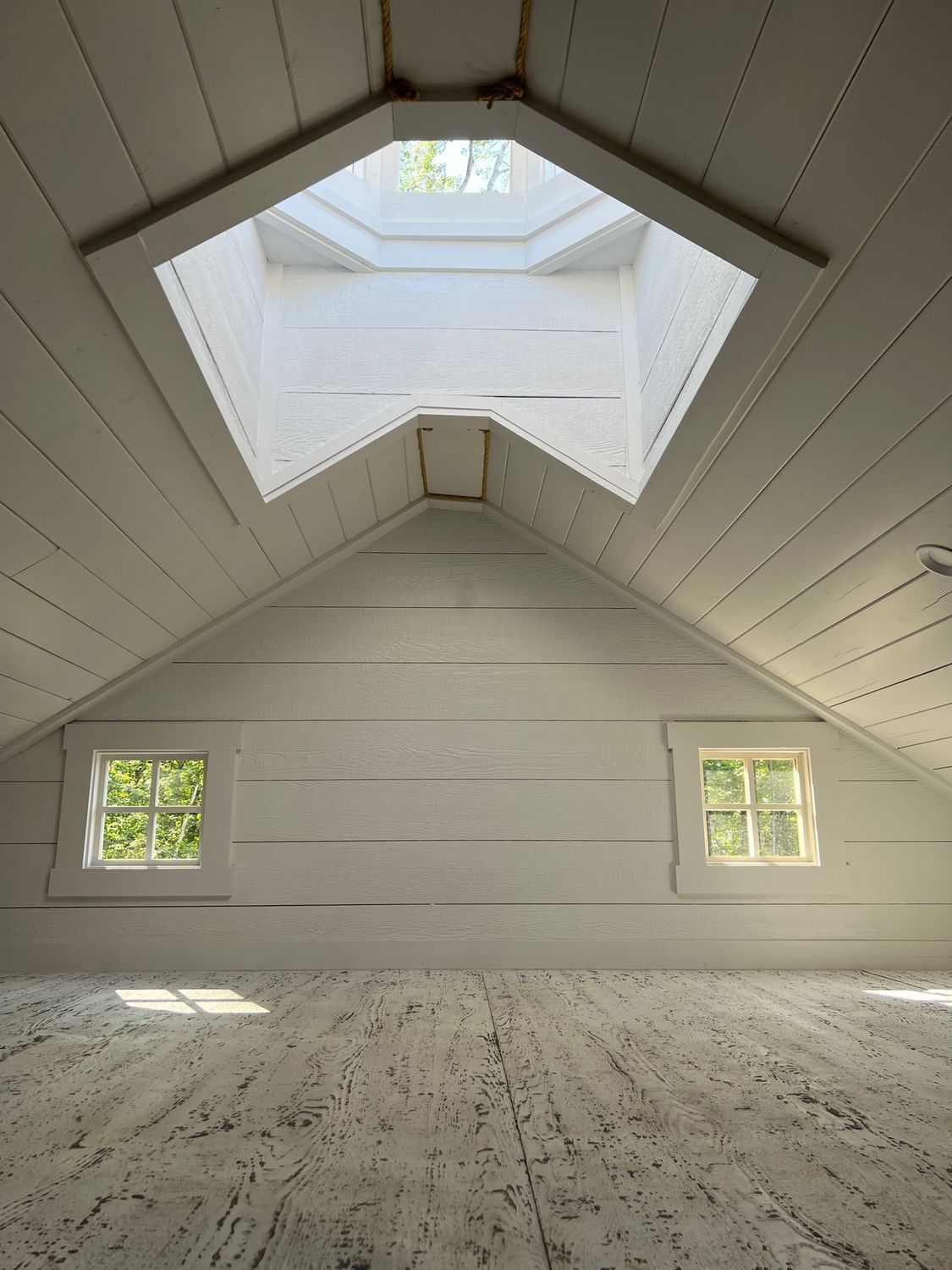 White attic interior with skylight and small windows; sunlight streams in.