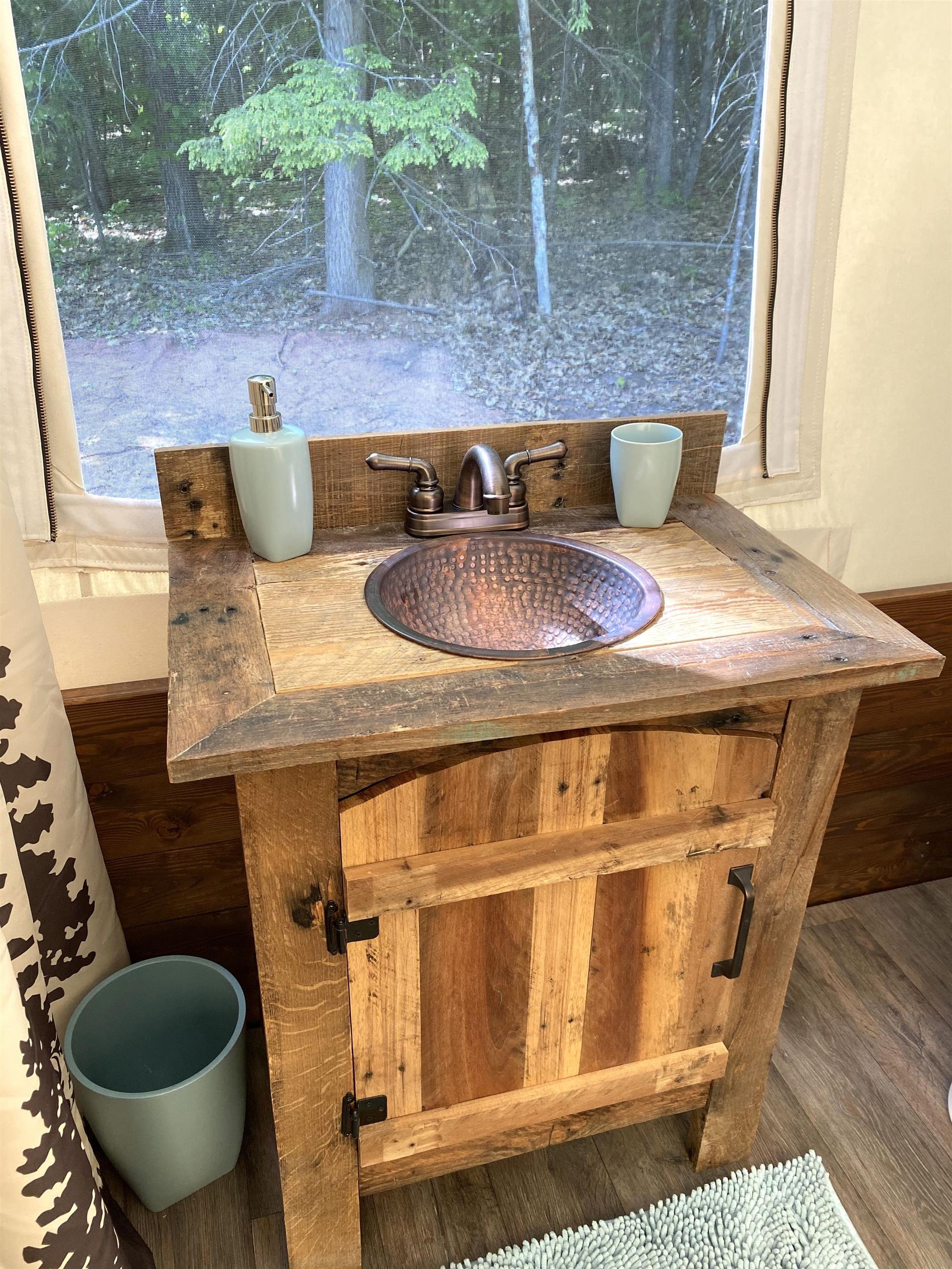 Rustic wooden vanity with copper sink, soap dispenser, and small window in the background.