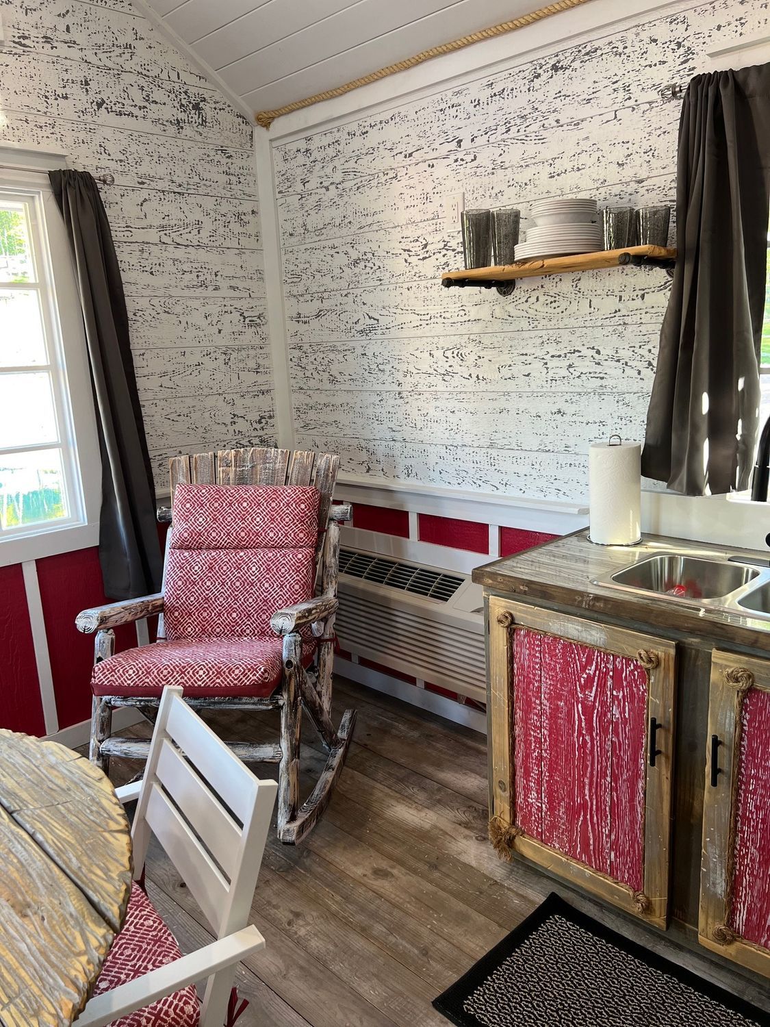 Red and white interior of a small cabin with a rocking chair, sink, and table.