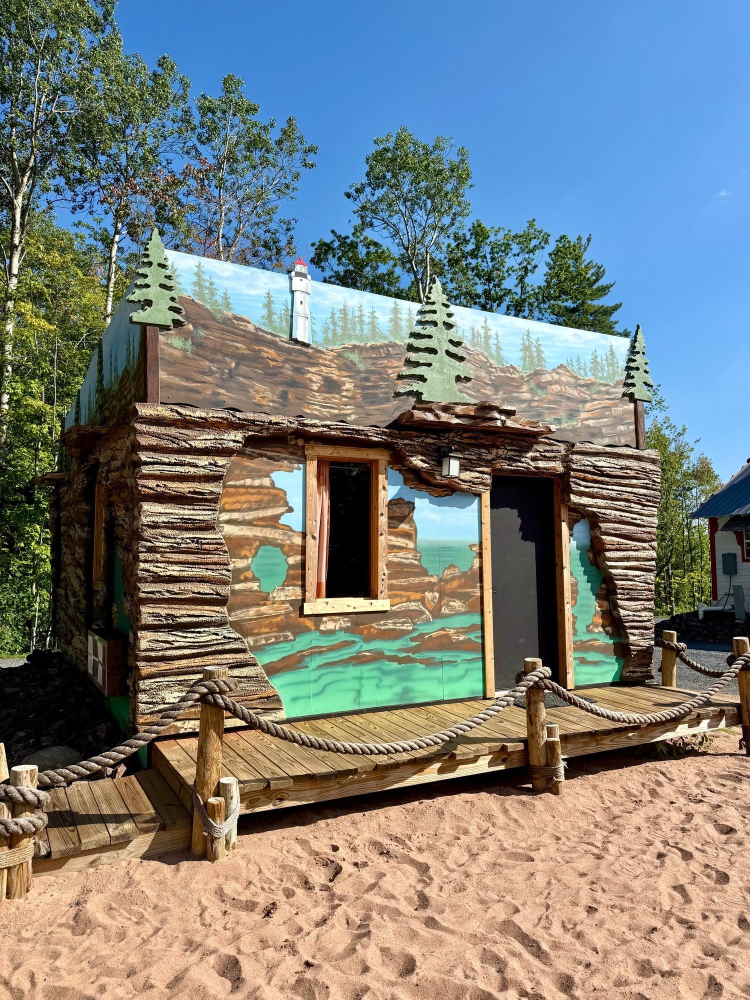 Cabin-shaped structure with brown wood-like walls, green and blue painted details, a small porch, and a blue sky.