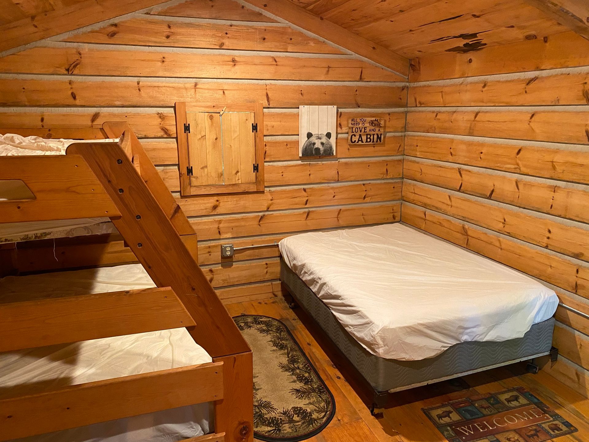 A small bedroom with bunk beds and a single bed; log walls, wooden trim, and a small rug.