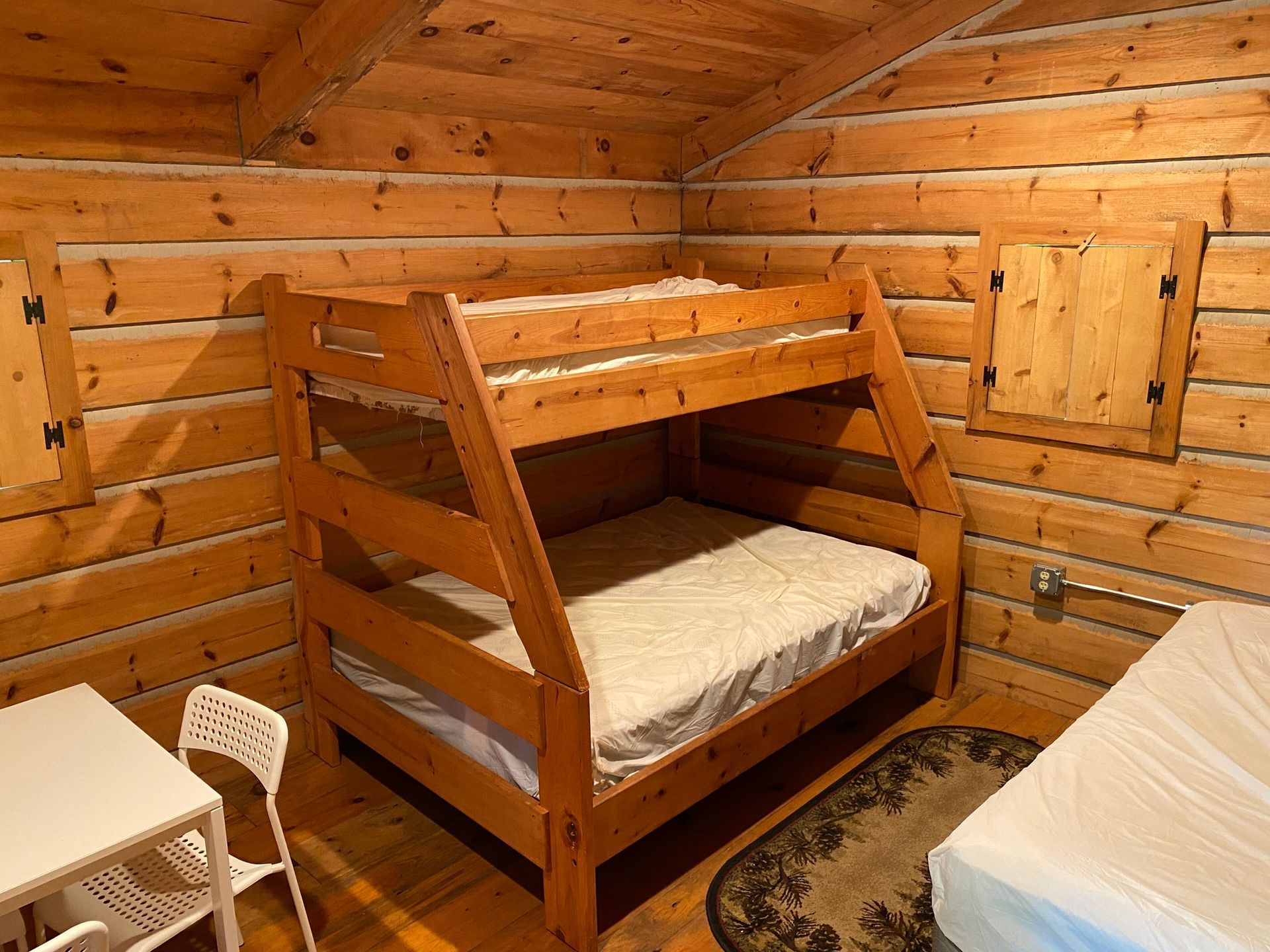 Bunk bed in a rustic room with wood paneling. A small table and a bed are also in the room.