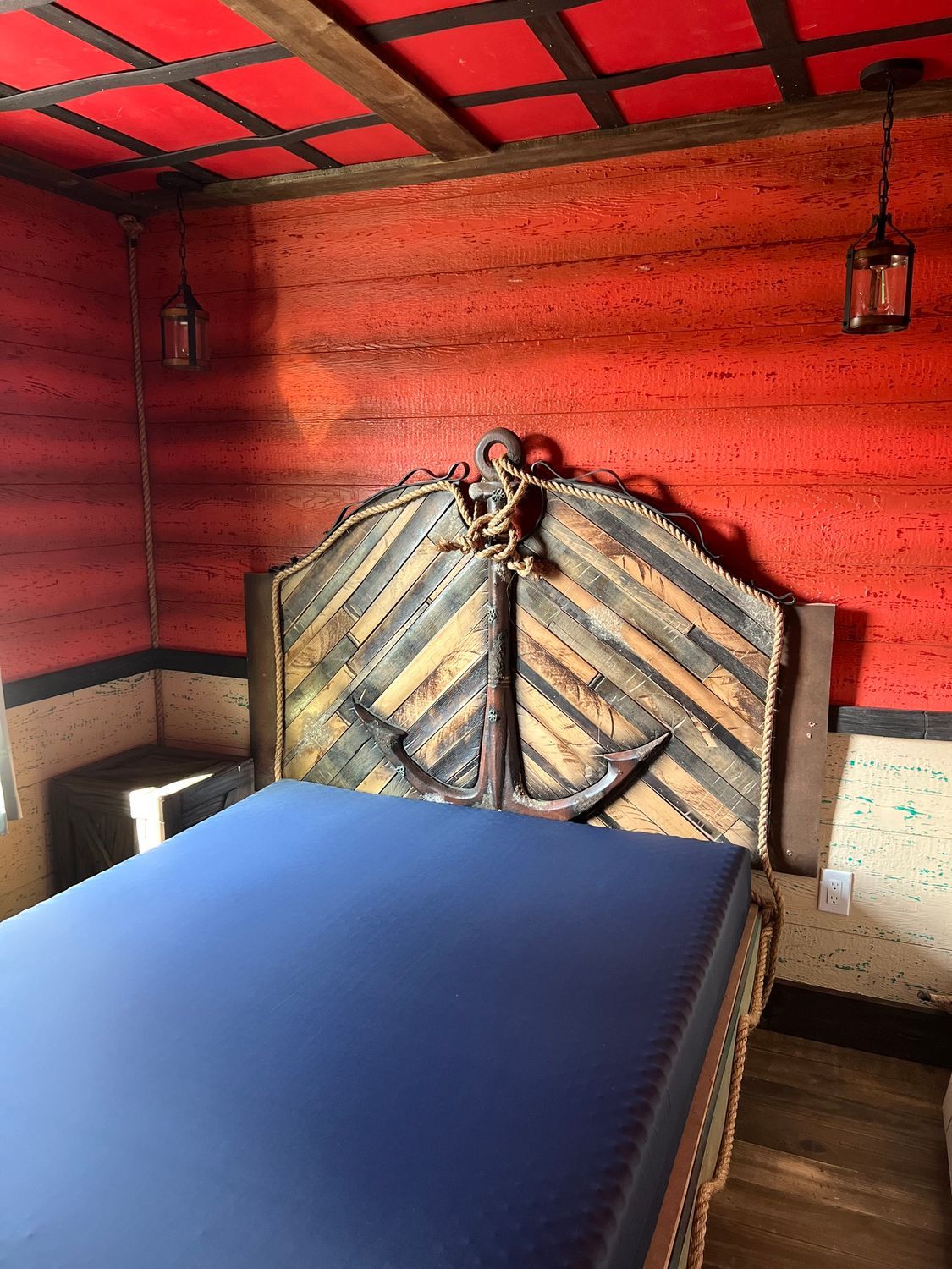 Bedroom with a nautical theme. Bed has a headboard shaped like an anchor. Red walls and ceiling.