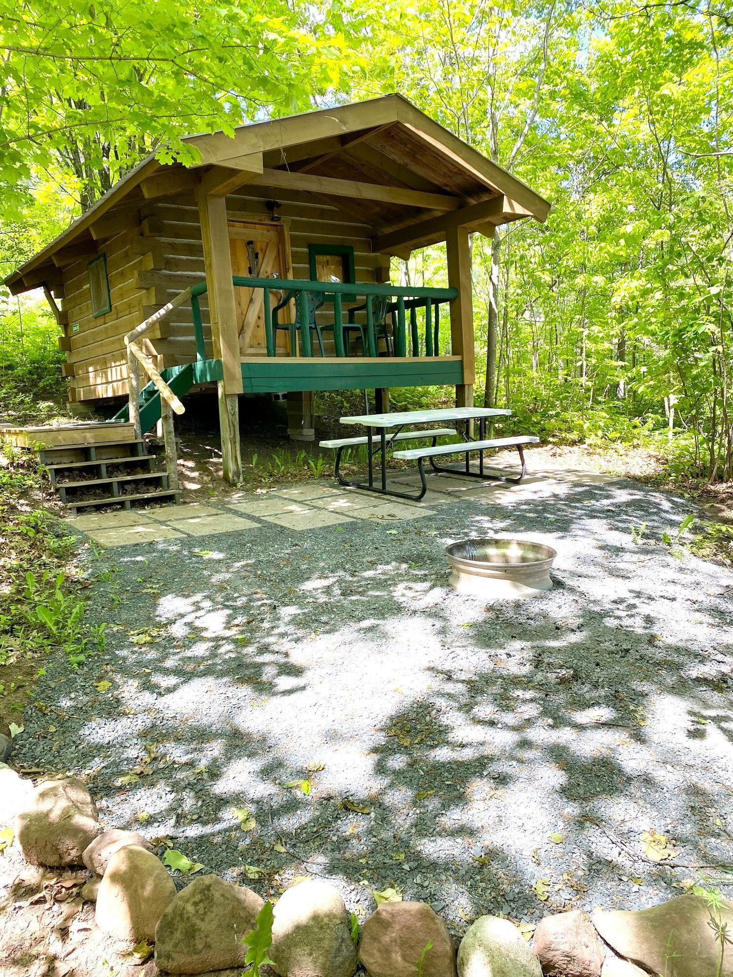 Cabin with porch, picnic table, and fire pit in a wooded area.