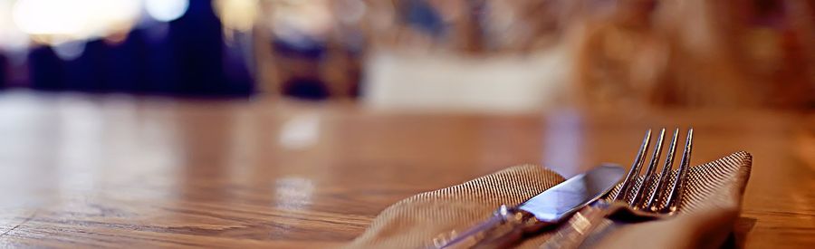 Fork and knife on a wooden table, blurry restaurant background.