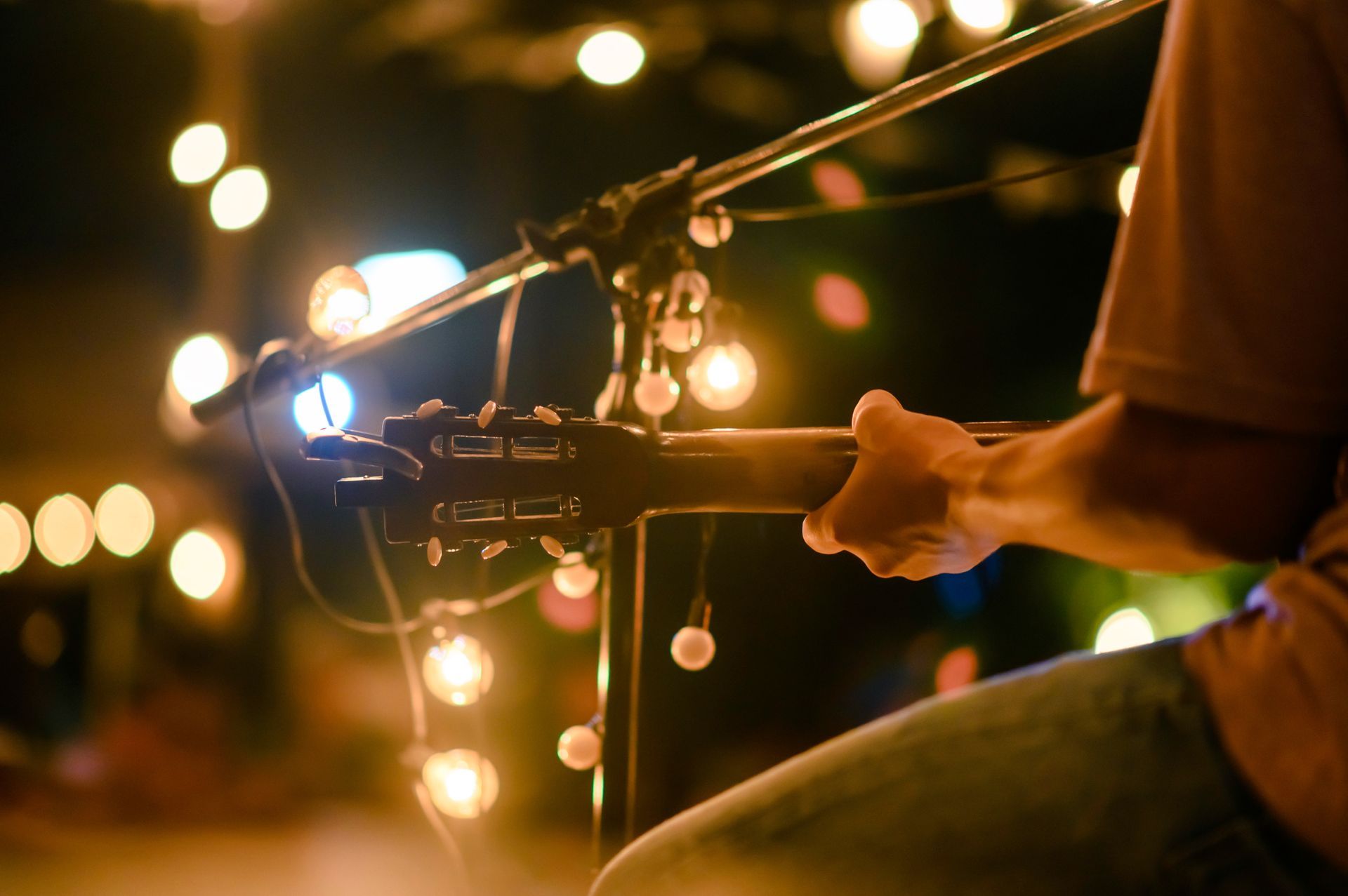 Guitarist playing with string lights in the background, out of focus.