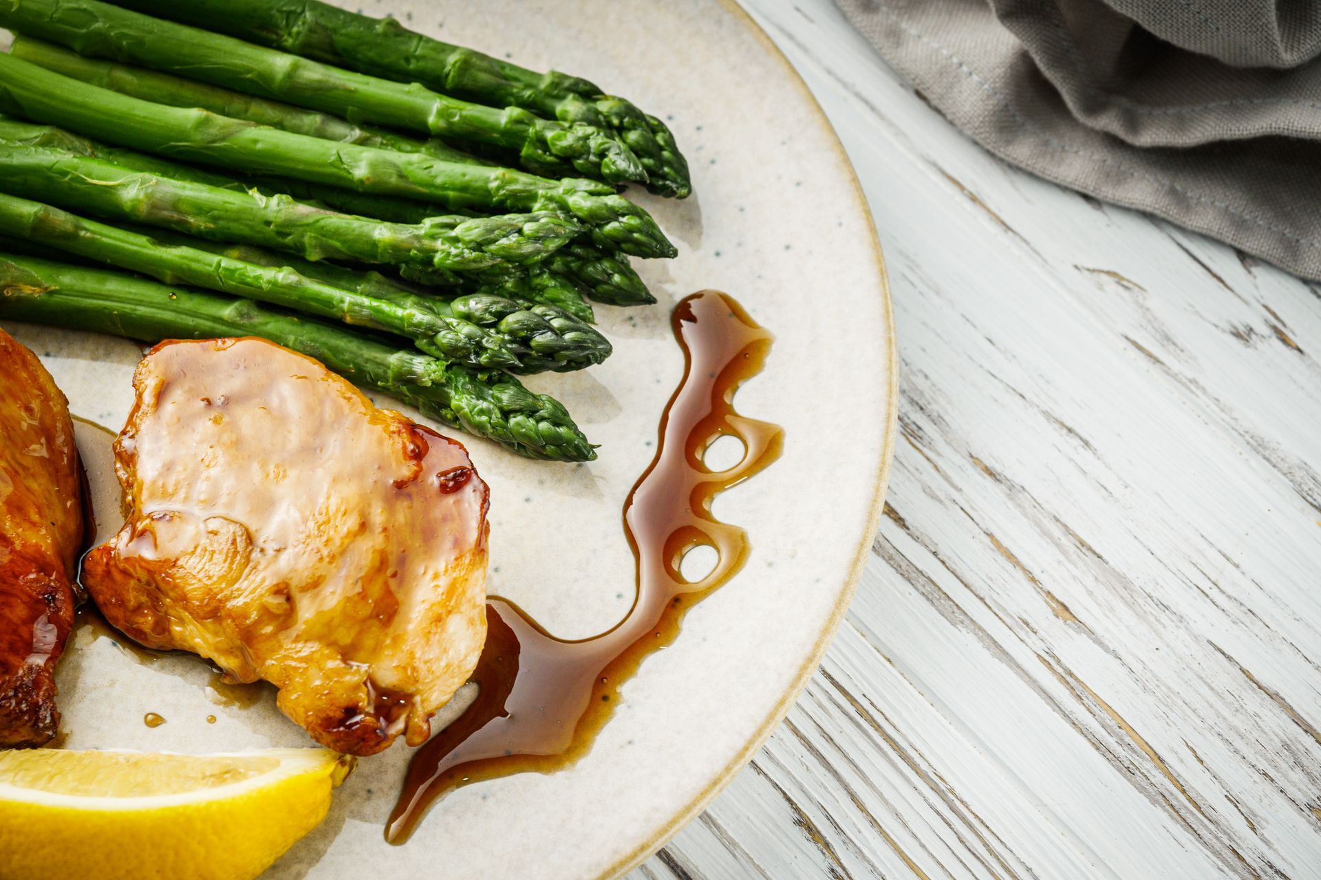 Plate with roasted chicken, asparagus, sauce, and a lemon wedge.
