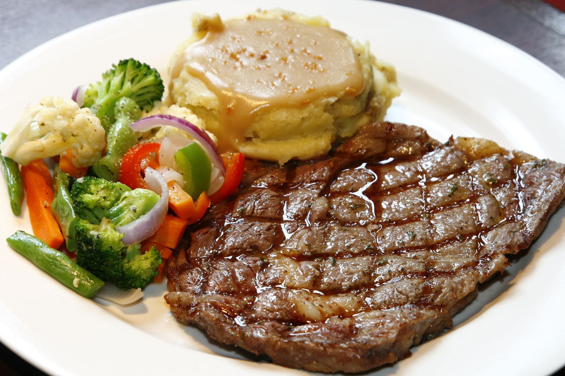 Grilled steak with mashed potatoes and vegetables on a white plate.