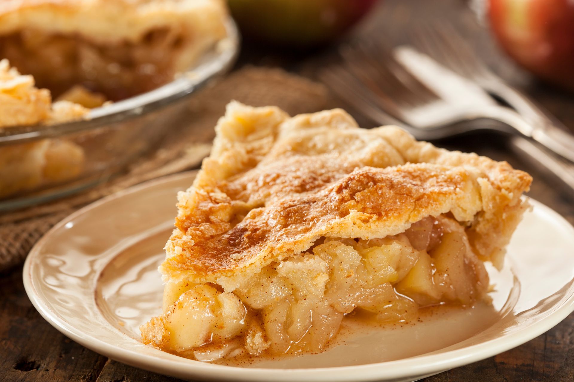 Slice of apple pie on a plate, close up. Golden crust, filling visible, wood background.
