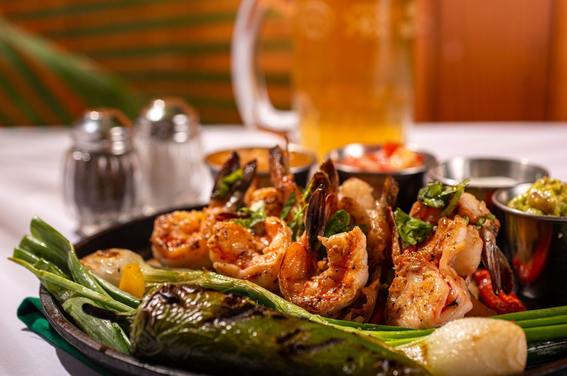 Sizzling shrimp fajitas with grilled vegetables, salsa, guacamole, salt and pepper shakers, and beer.