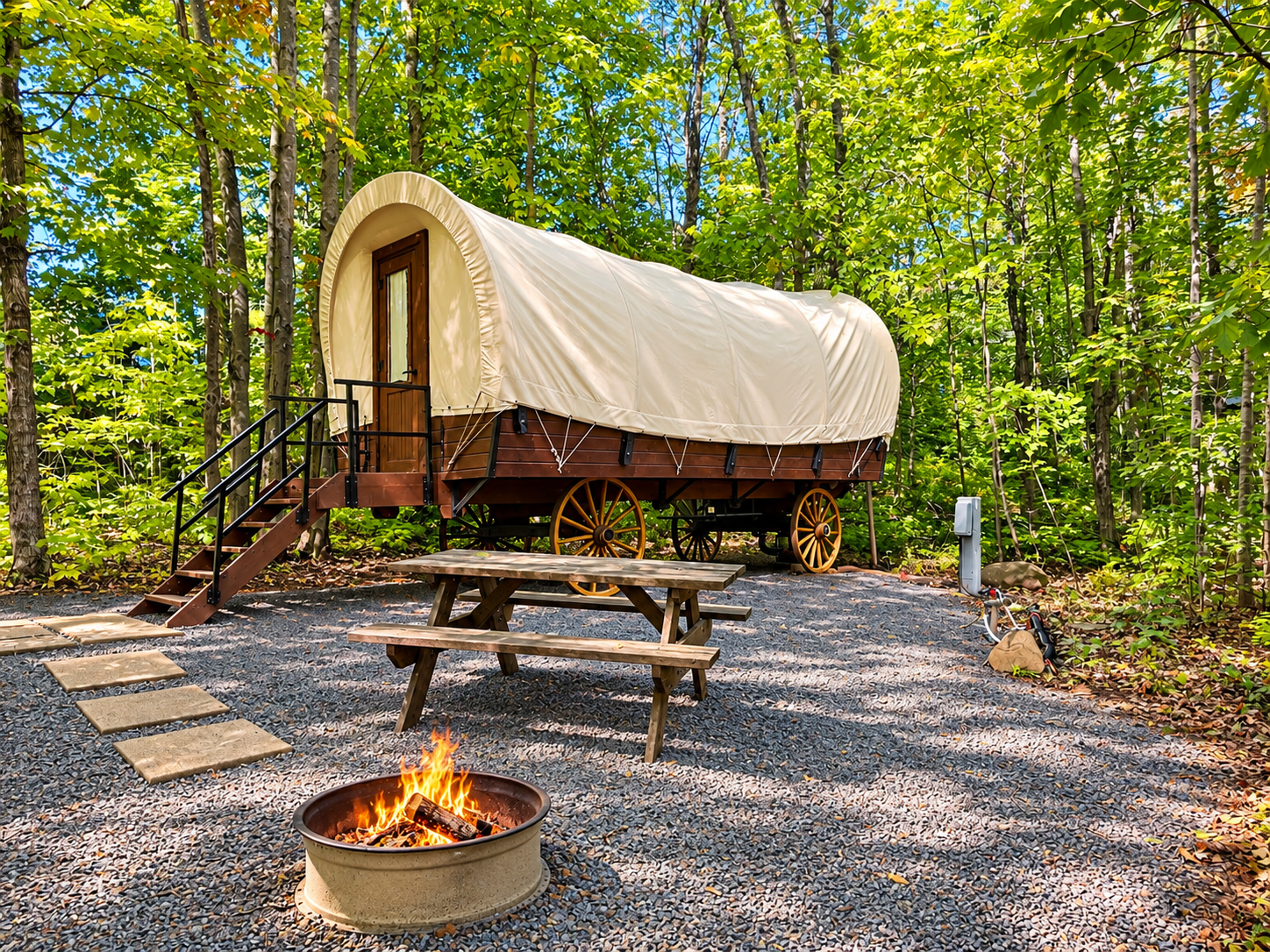 Covered wagon campsite, steps, small picnic table with food/drinks, fire pit, forest background.