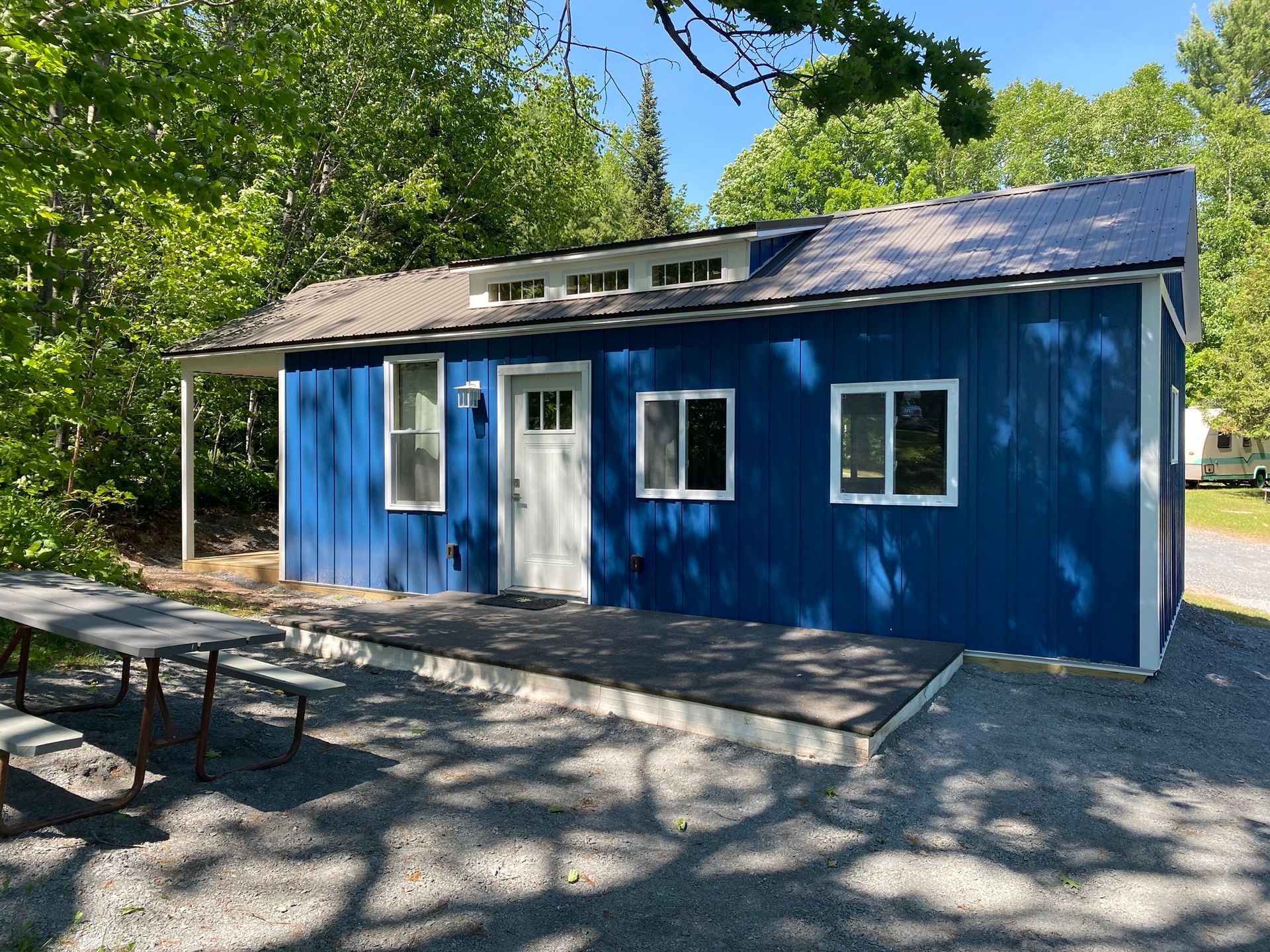 Blue cabin with white door, windows, and small porch; picnic table in front.