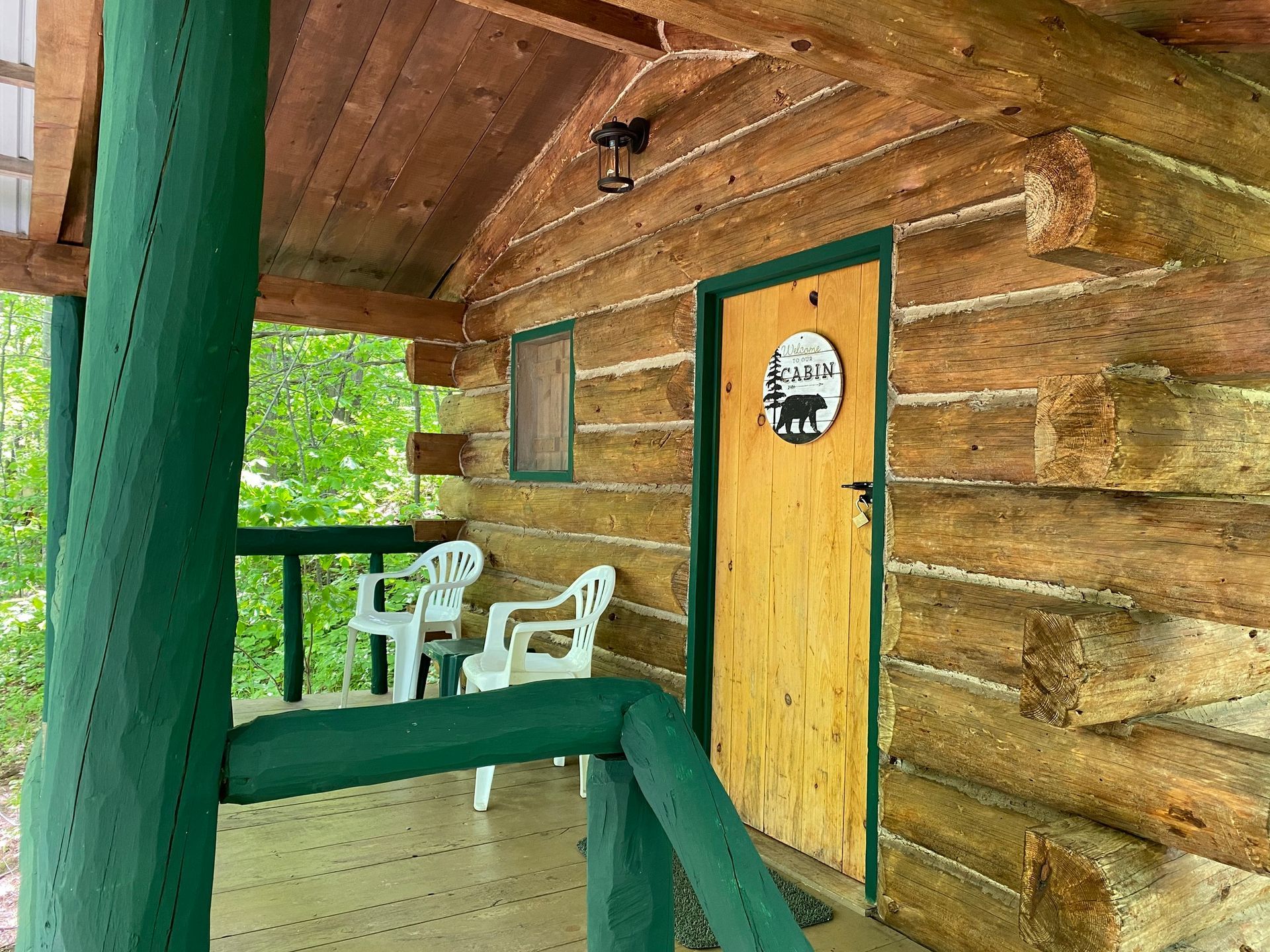 Porch of a log cabin with two white chairs, green railing, and a door with a bear sign.