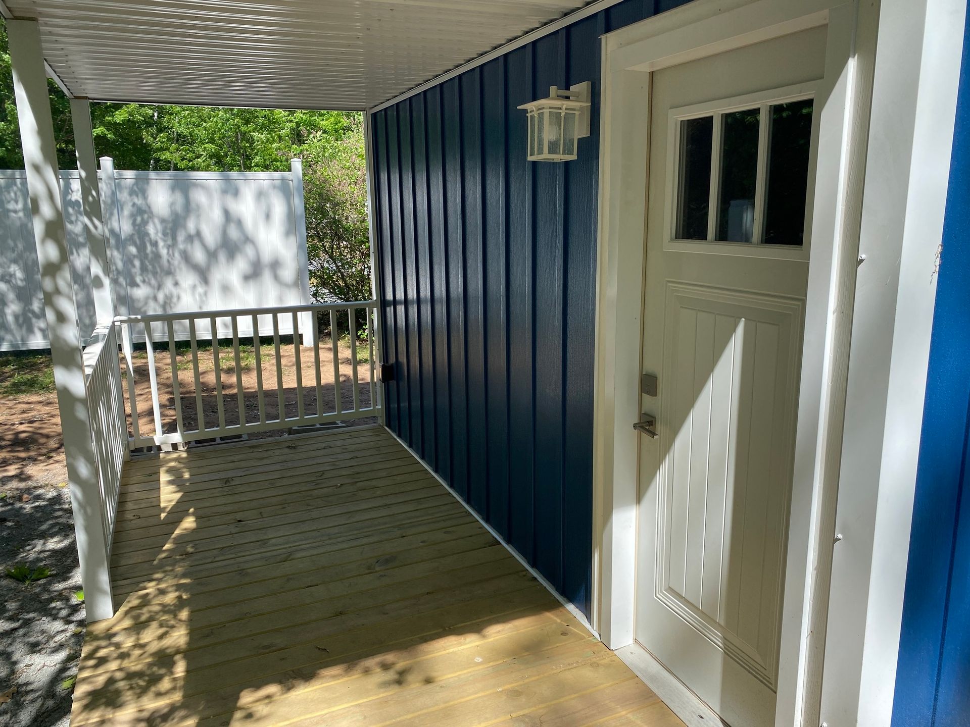 Blue building exterior with white trim, porch, and door. Shadowed wooden deck.