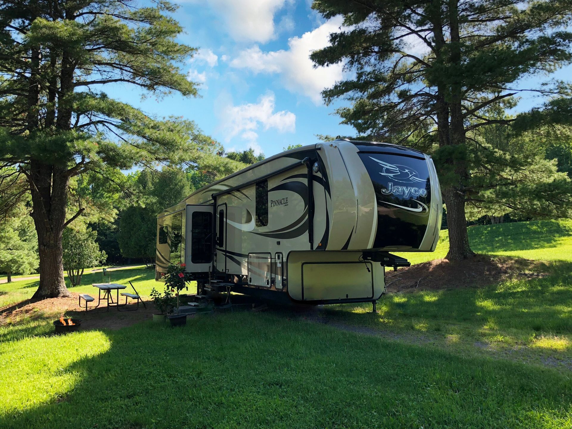 RV parked on grass in a campground with trees, awning extended, and picnic table.