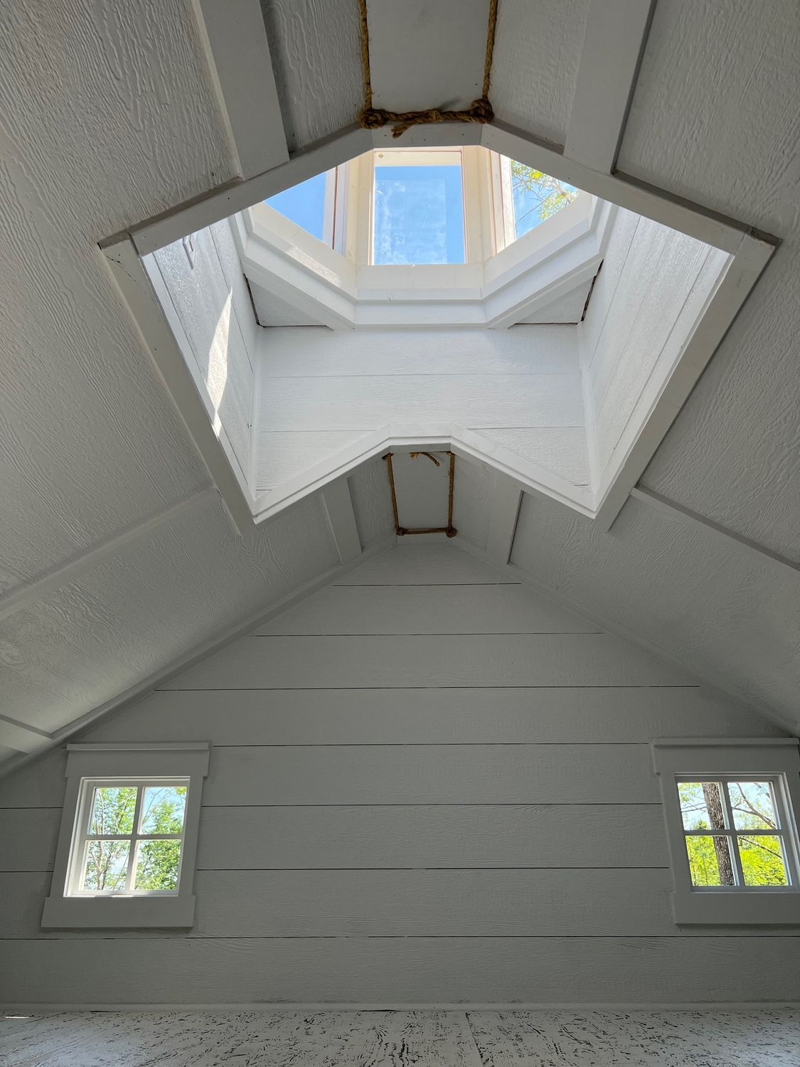 Interior of a white-painted attic with a skylight, two small windows, and sloped walls.