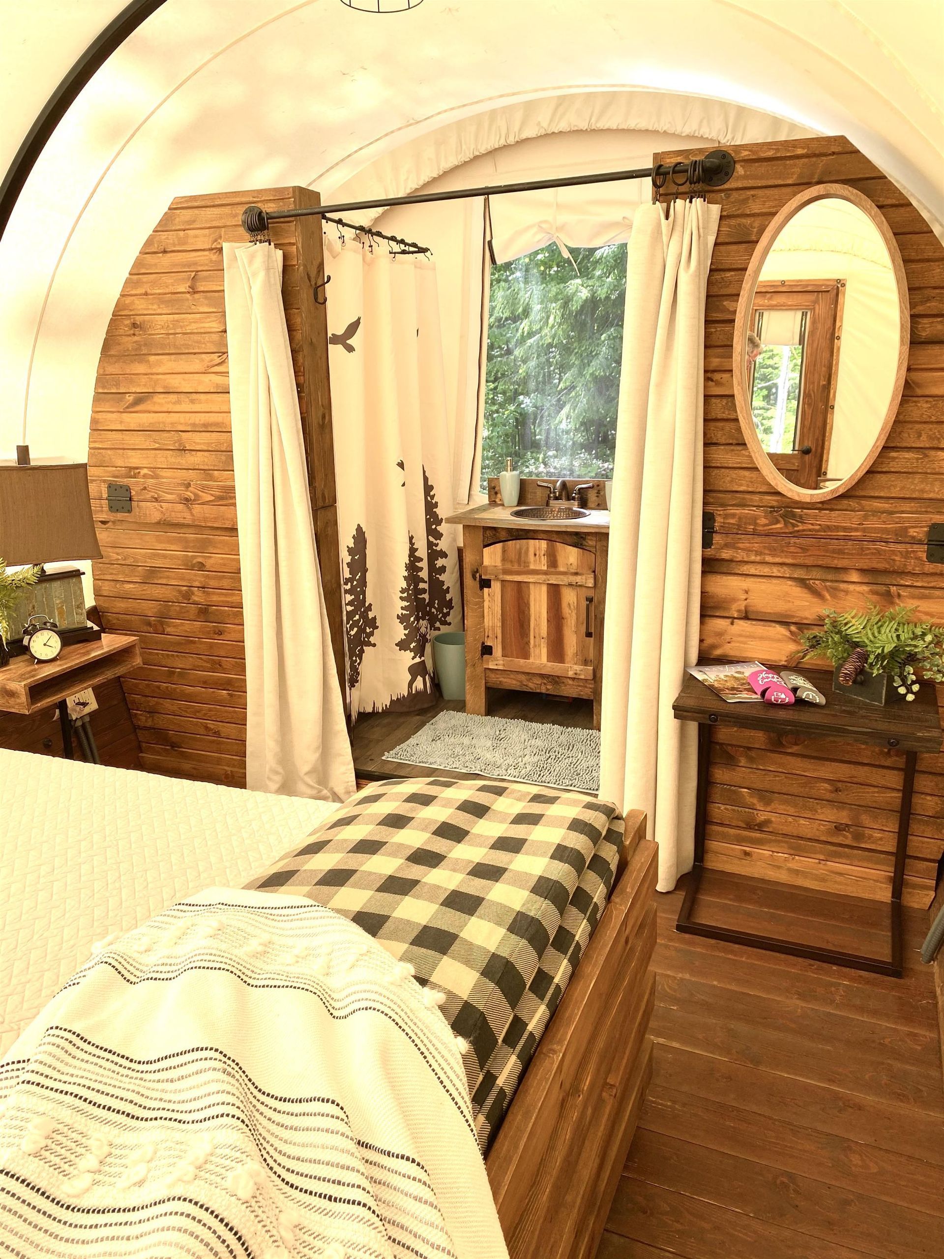 Interior of a rustic wagon-style cabin bedroom with wooden walls and bed. View to an open doorway with a sink and a mirror.