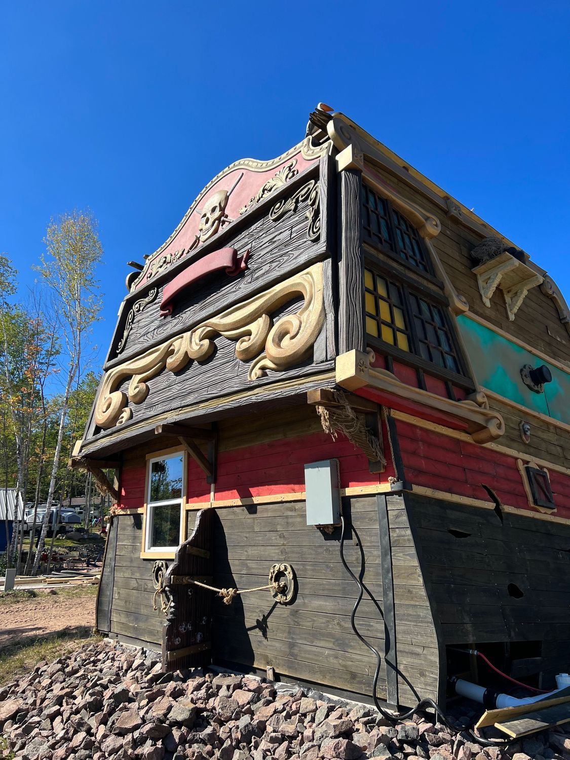 Exterior view of a pirate ship-themed building with red and black siding. Features decorative carvings and a small window.