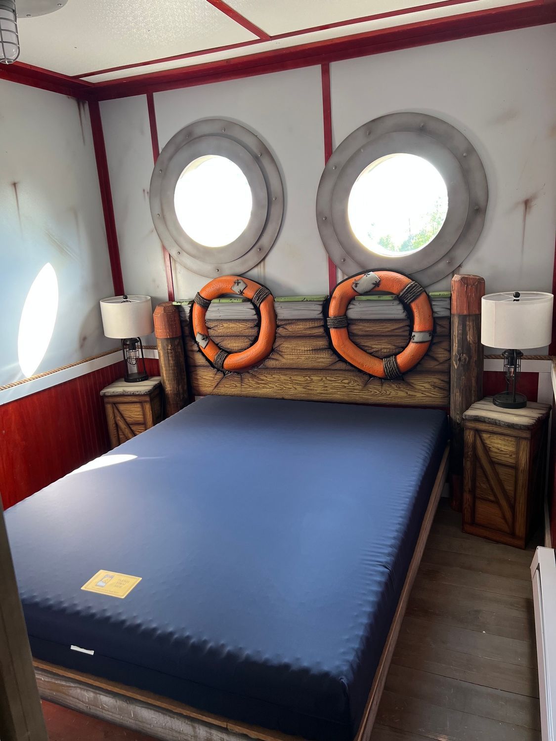 Bedroom with porthole windows, nautical-themed headboard, blue mattress, and two nightstands.