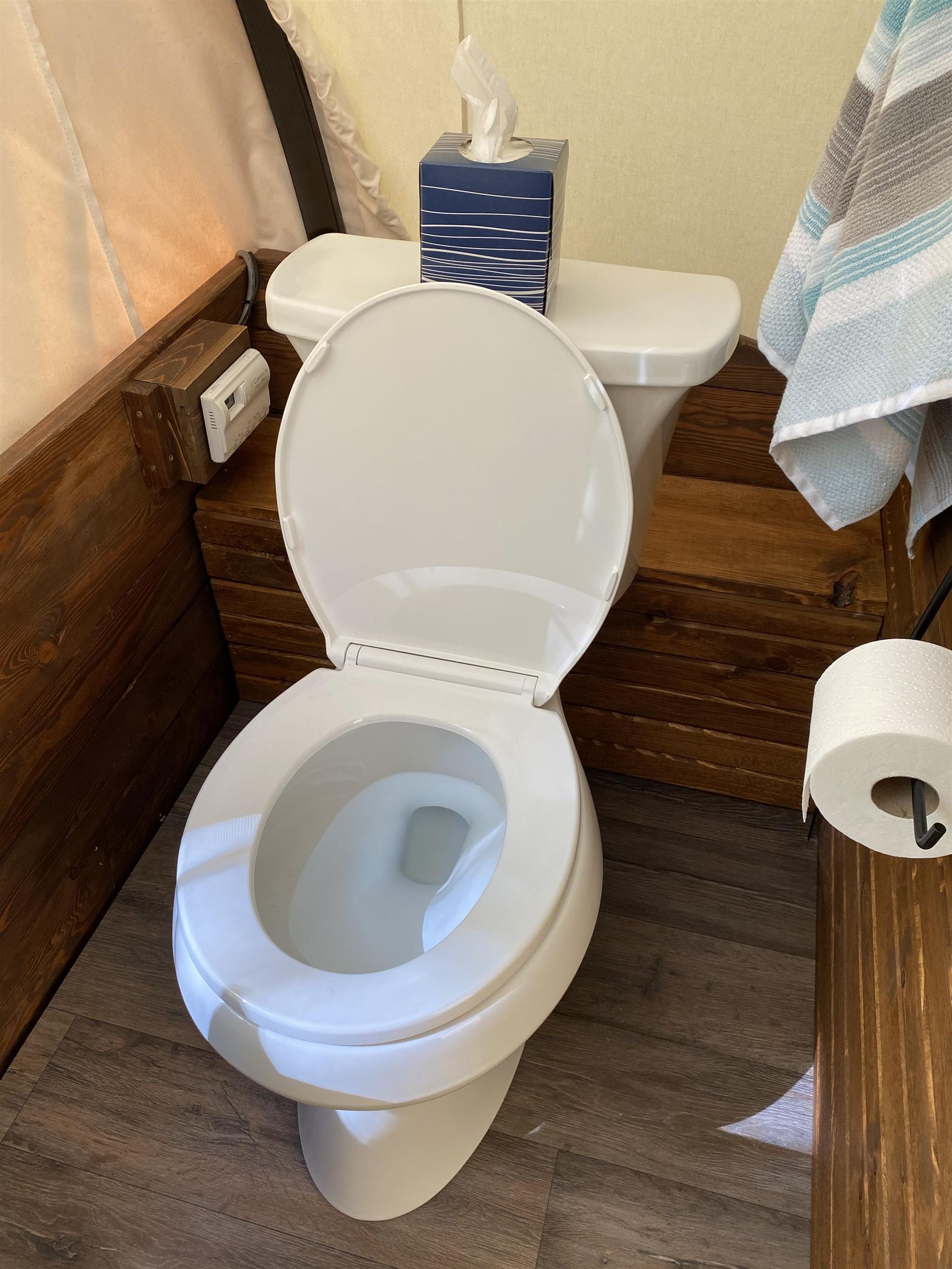 White toilet with open seat, tissue box, and towel.