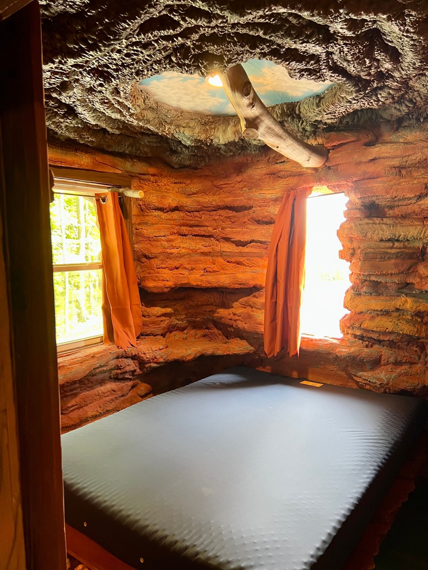 Cozy bedroom built into rock. Bed, curtains, and windows with light streaming in.
