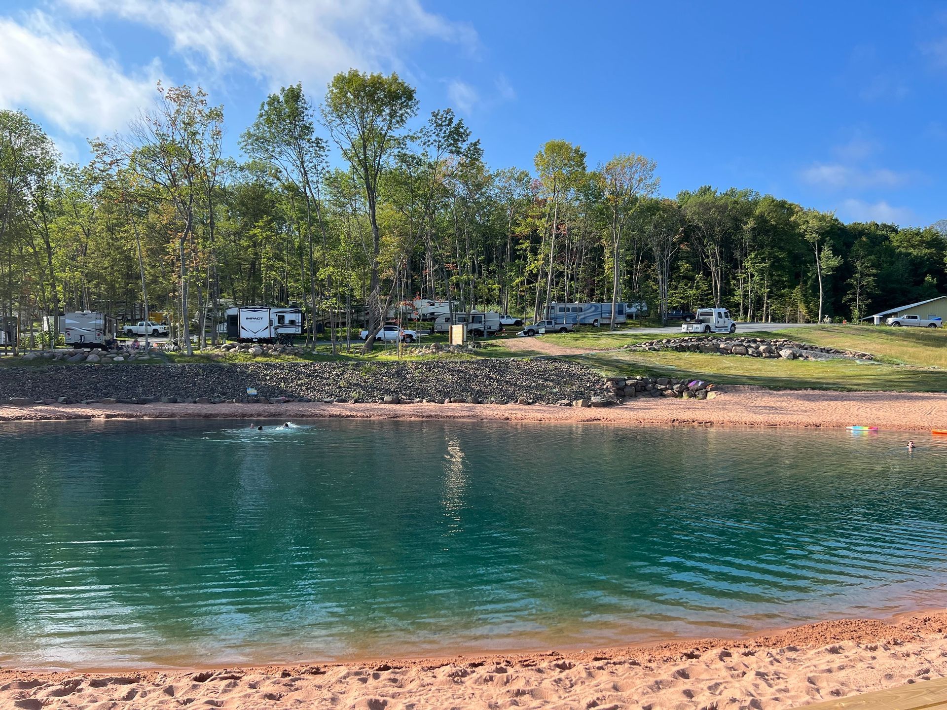 Campsite beside a blue lake; RVs and trees line the shore under a blue sky.
