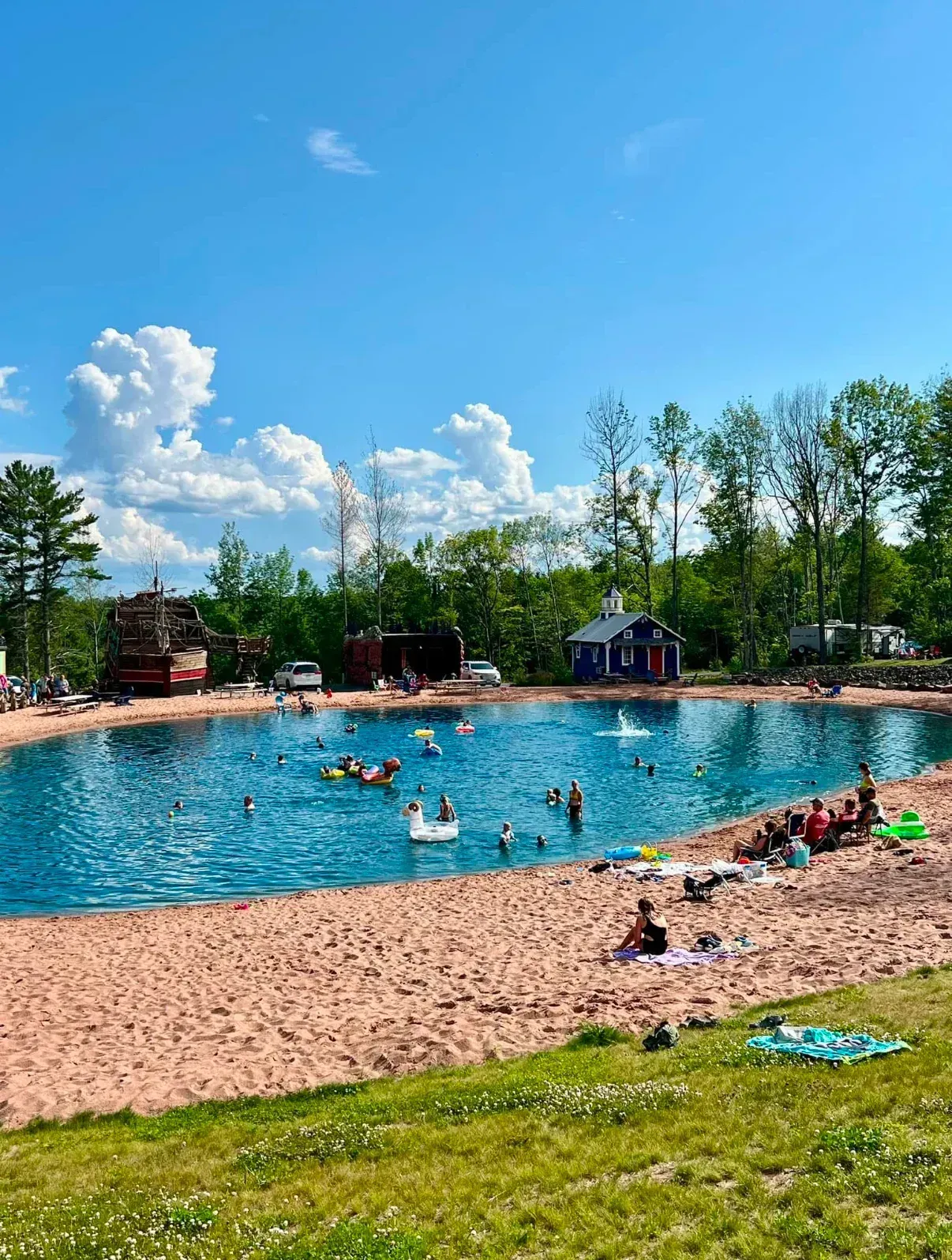 People swim and relax in a blue lagoon with a sandy beach on a sunny day.
