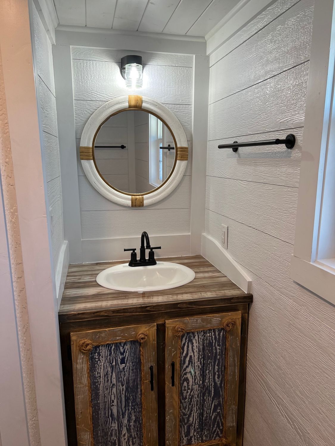 Bathroom with a round mirror, wooden vanity, and white paneling.