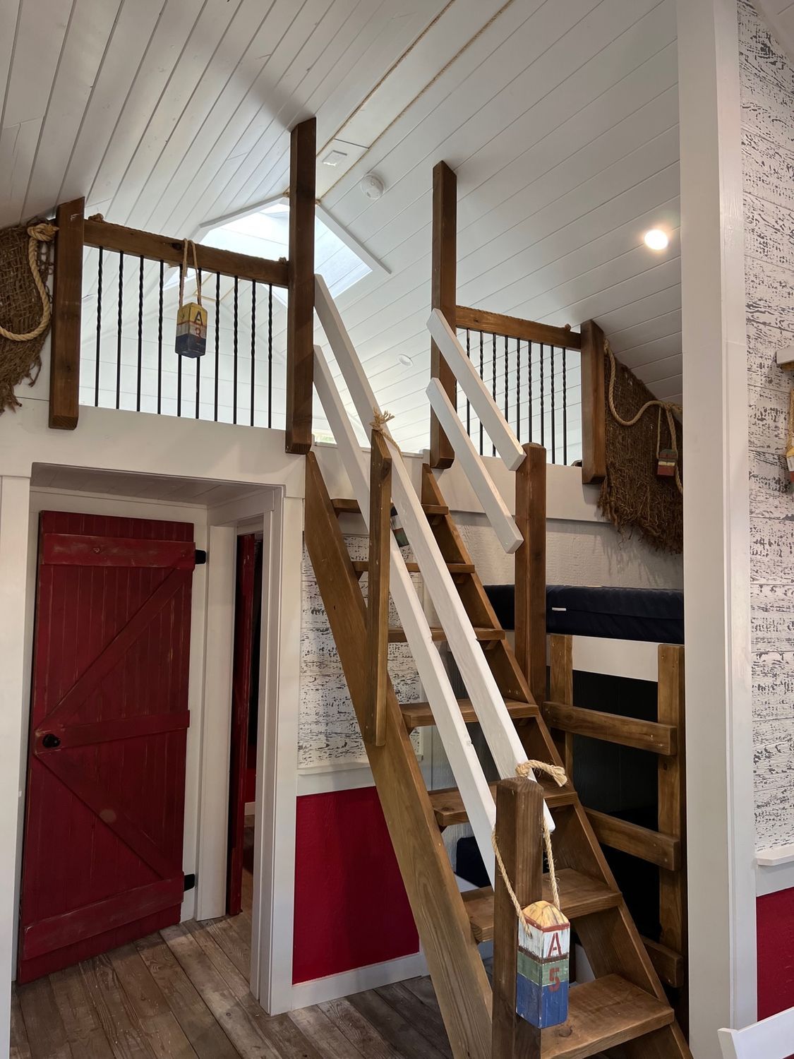 Interior with loft, wooden staircase, red door, white walls, and skylight.