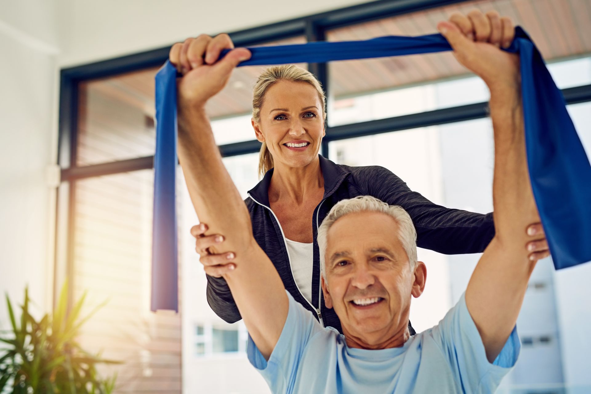 A therapist assists a patient with shoulder stretching exercises using a blue resistance band in a bright, modern room.