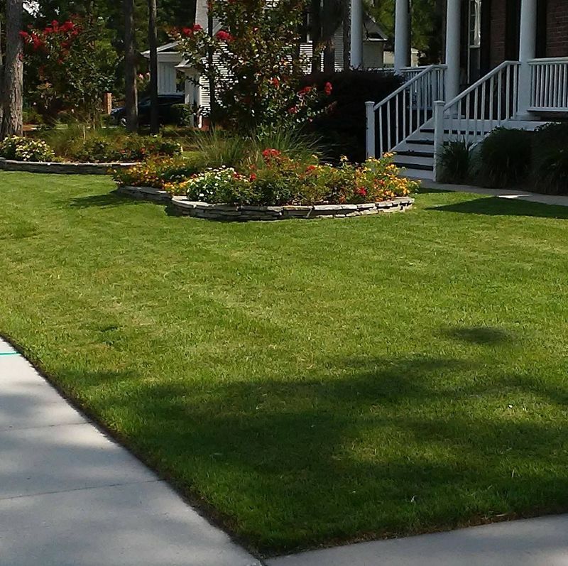 Front yard with green lawn, flower beds, and white porch steps beside a sidewalk