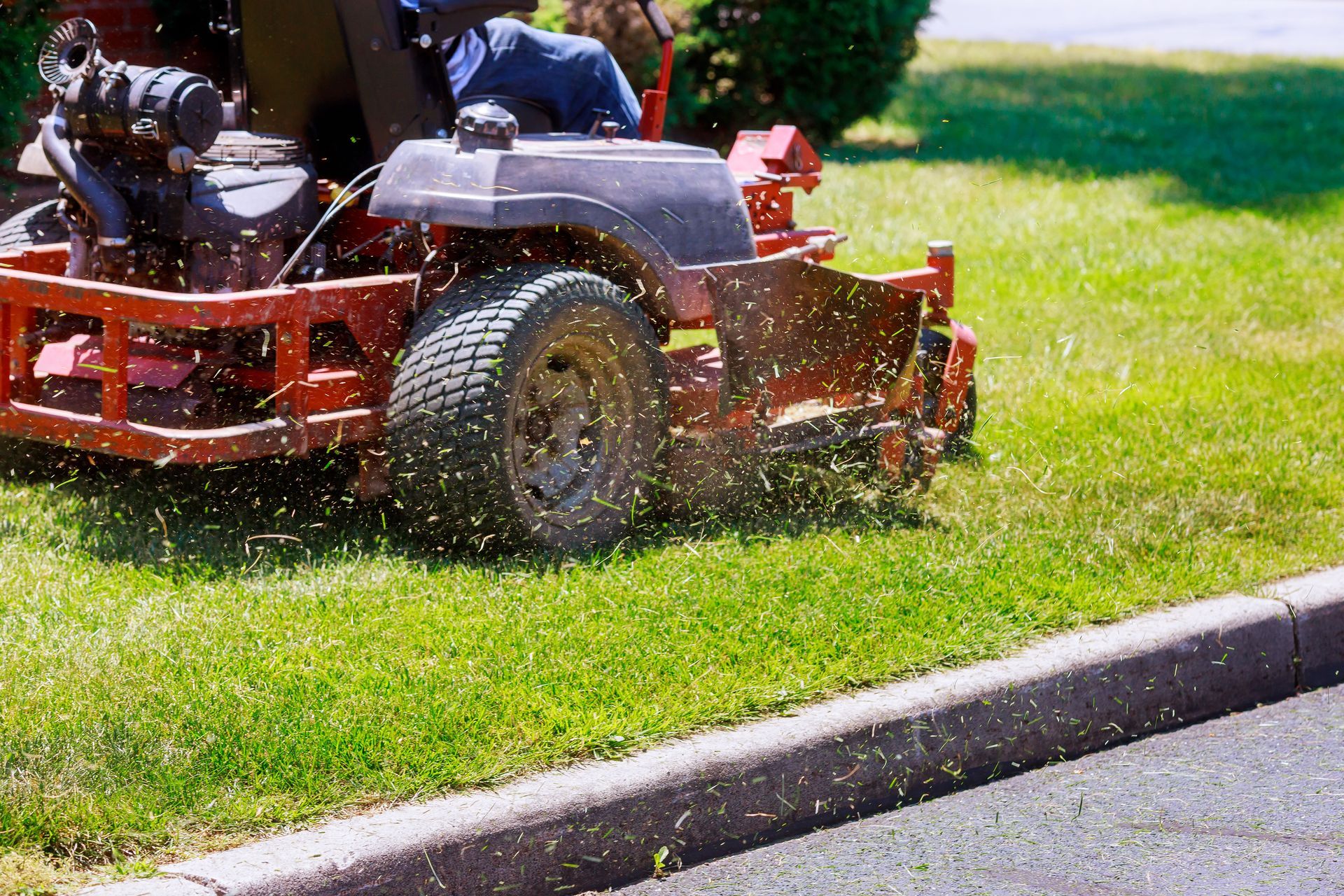 Red riding lawn mower cutting grass beside a curb on a sunny day