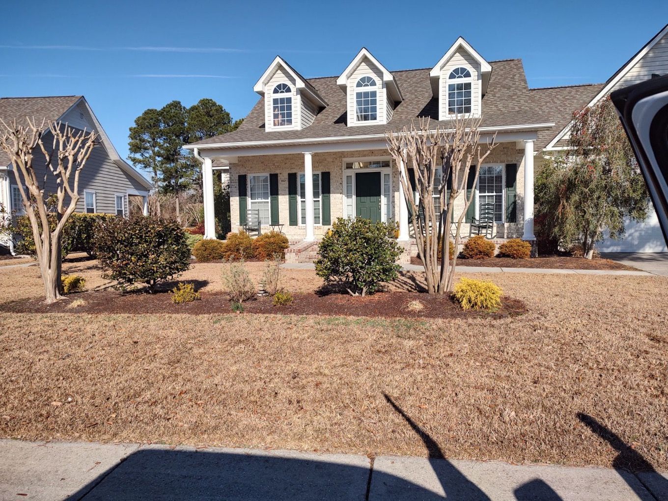 Suburban house with white columns, dormer windows, and a gravel front yard under a clear blue sky