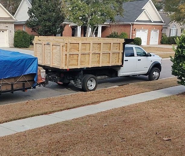 White pickup truck carrying a large wooden crate parked on a suburban street beside a blue-covered trailer.
