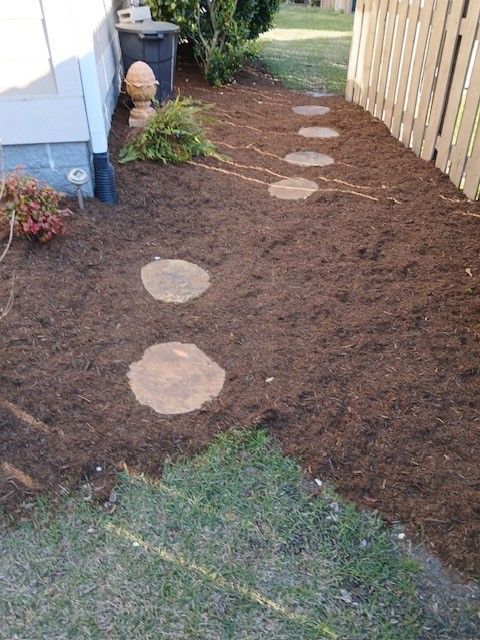Garden path with round stepping stones through fresh mulch beside a house and wooden fence