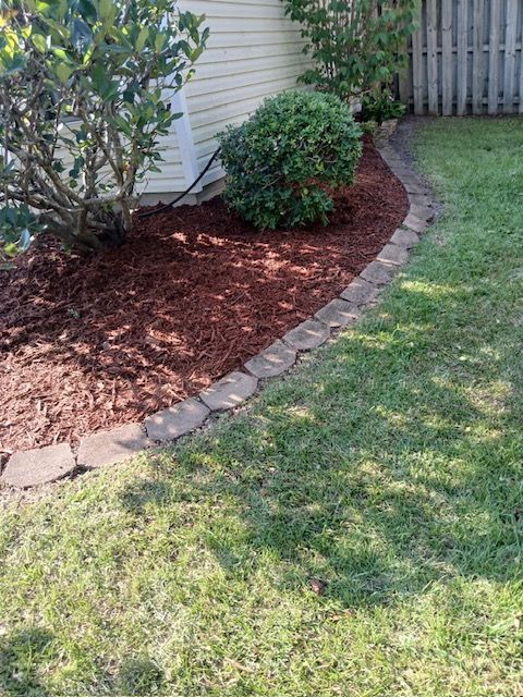 Mulched flower bed with shrubs and brick edging beside a house and green lawn