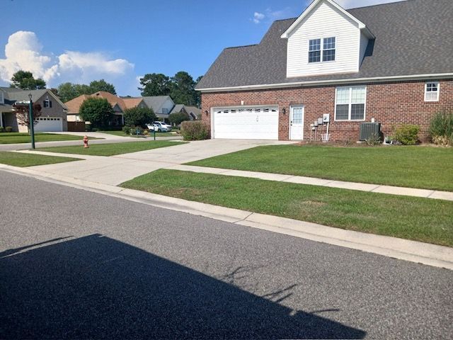 Suburban street with brick house, driveway, lawn, and partly cloudy sky