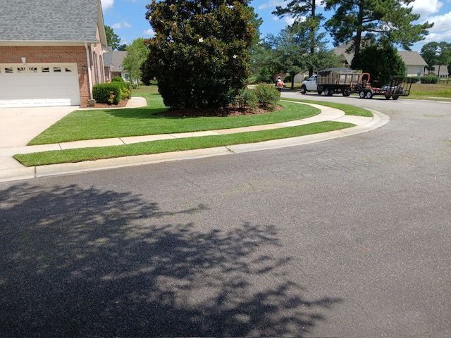 Suburban street corner with a curved sidewalk, green lawn, trees, and a house garage on a sunny day