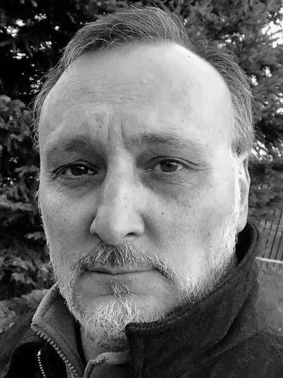 Black-and-white close-up portrait of a man with a serious expression outdoors.