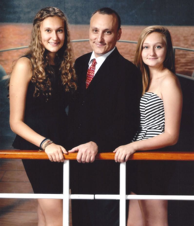 Three people posing by a railing, with two women flanking a man in a suit, against a dark backdrop.