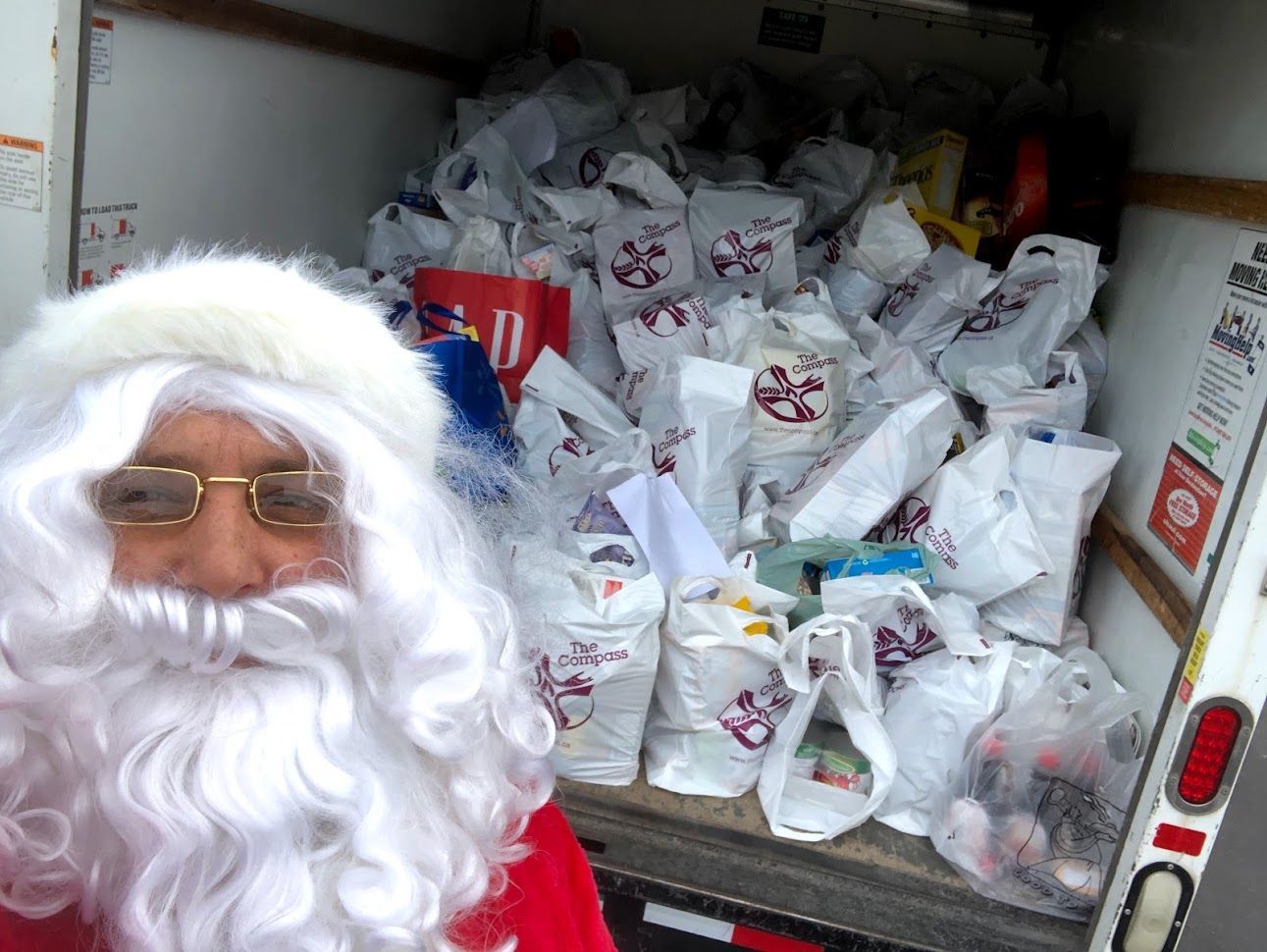 Person in Santa costume in front of a truck packed with Food Donations