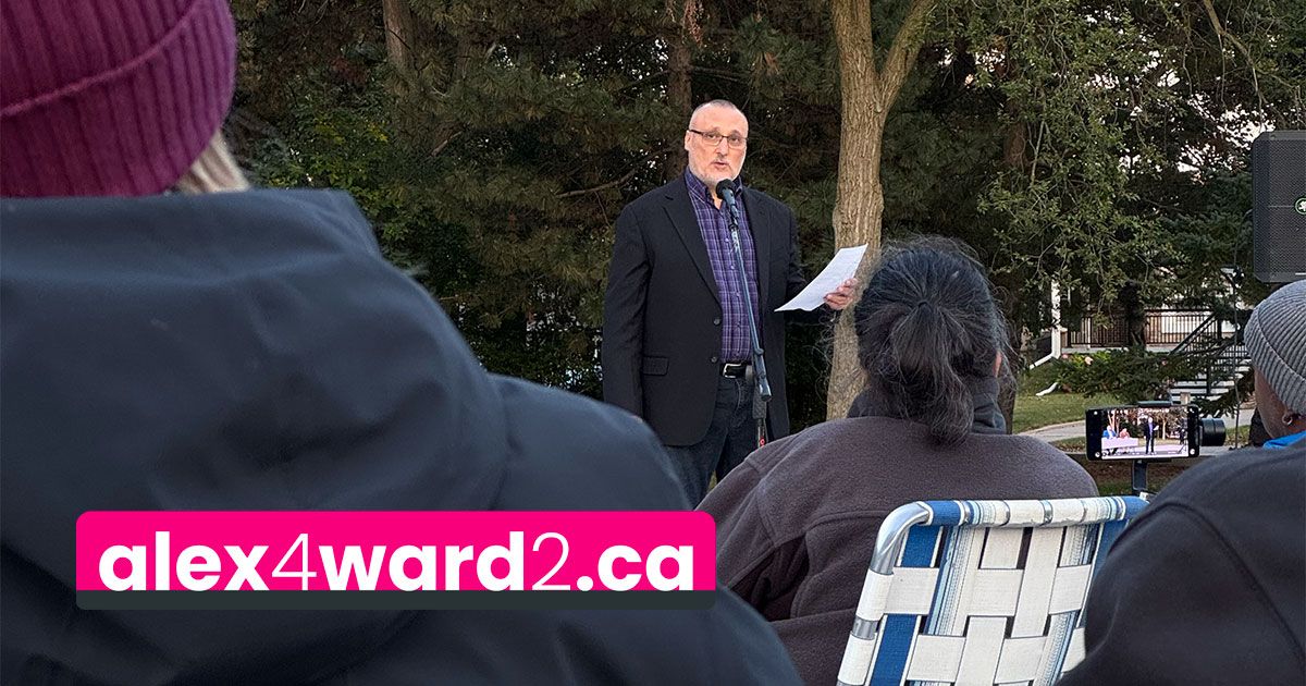 Outdoor speaker at a small gathering, speaking to seated audience in a park; alex4ward2.ca banner in foreground