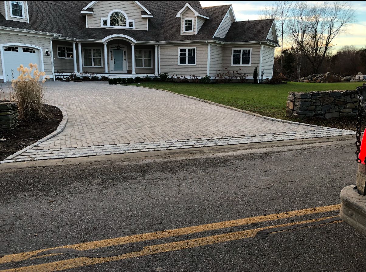 House with a wide cobblestone driveway and front lawn beside a road at dusk