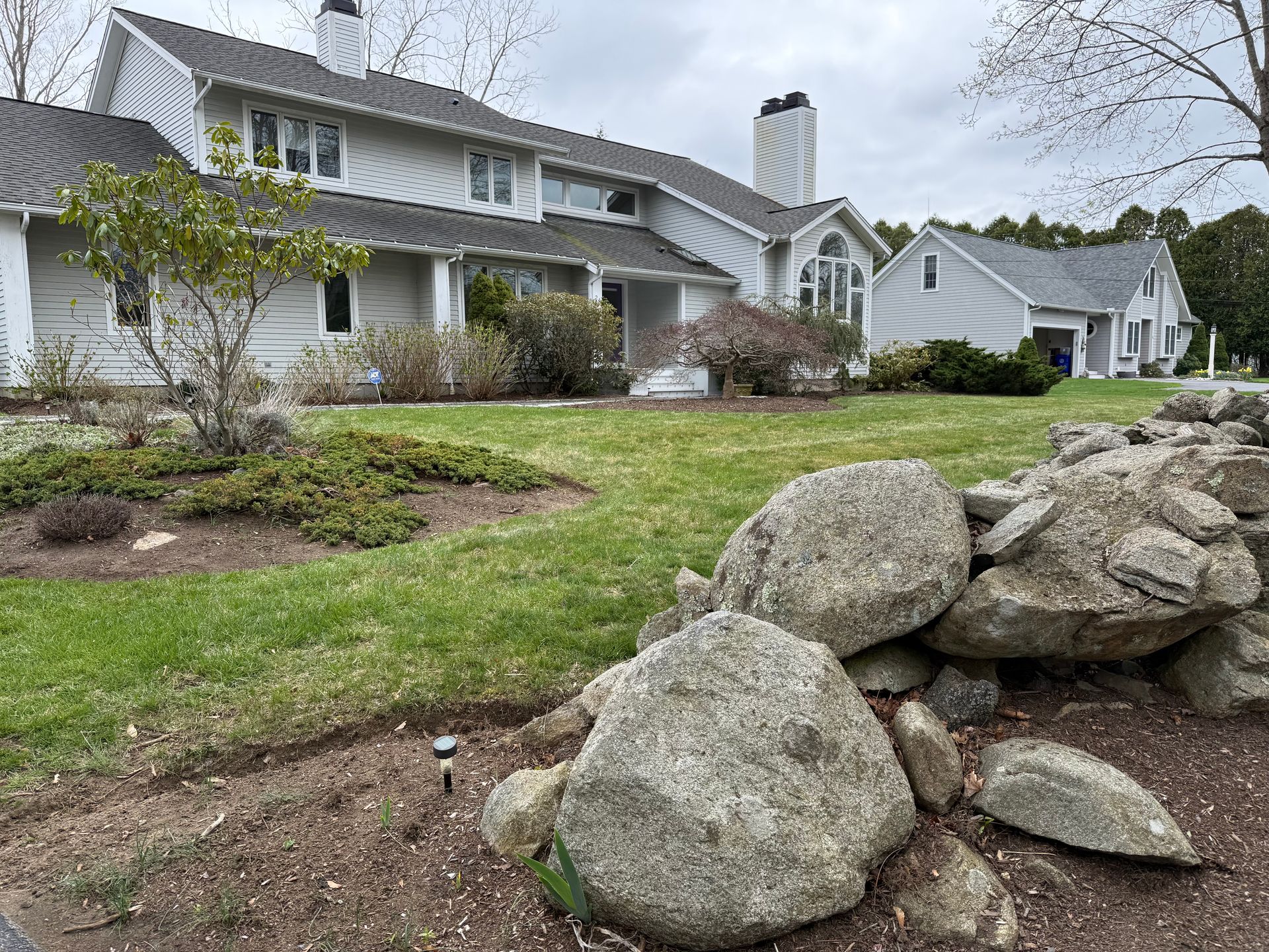 Suburban houses with a grassy front yard and large rock landscaping in the foreground