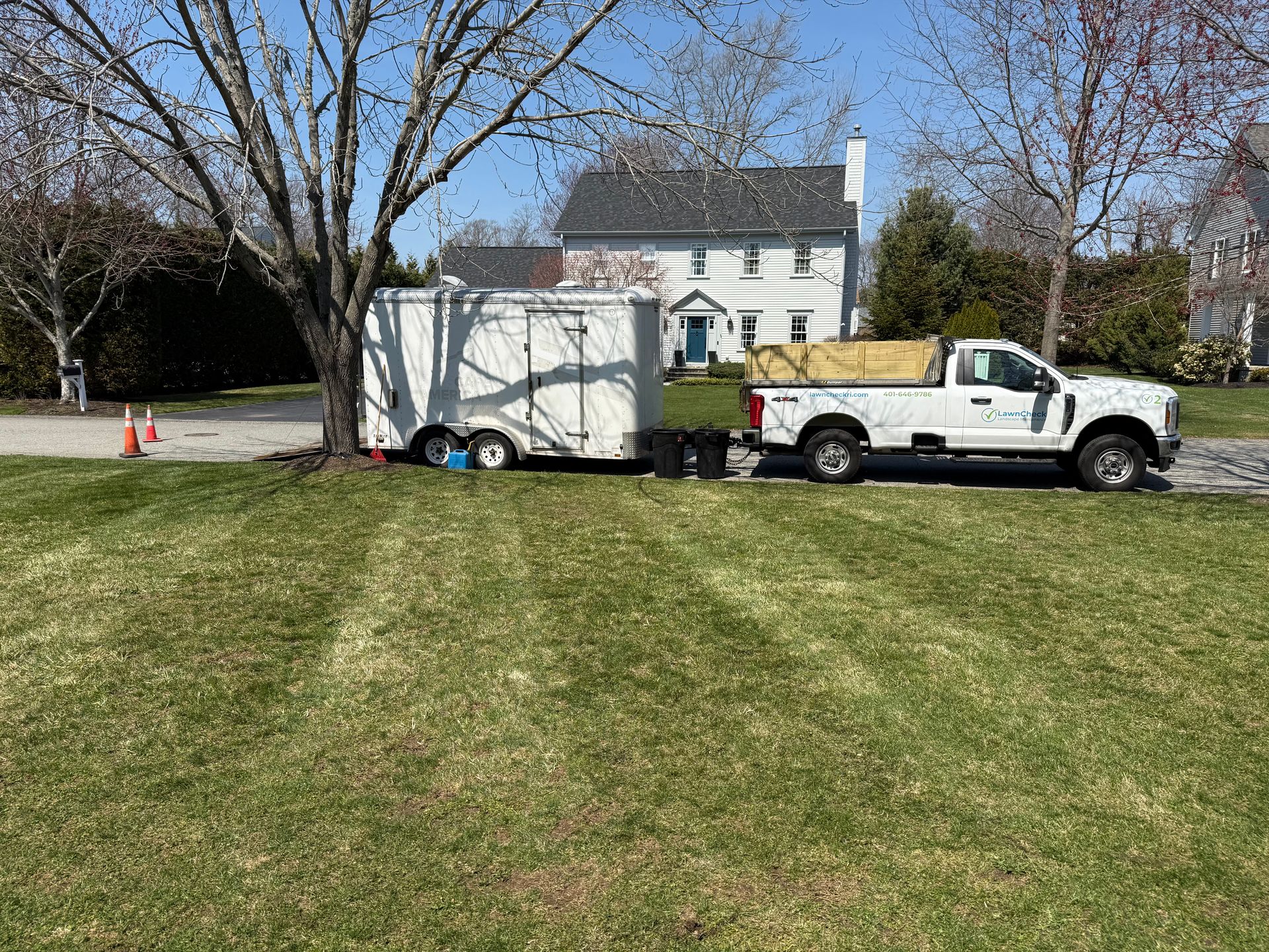 White truck towing a small trailer on a grassy lawn near a house and trees