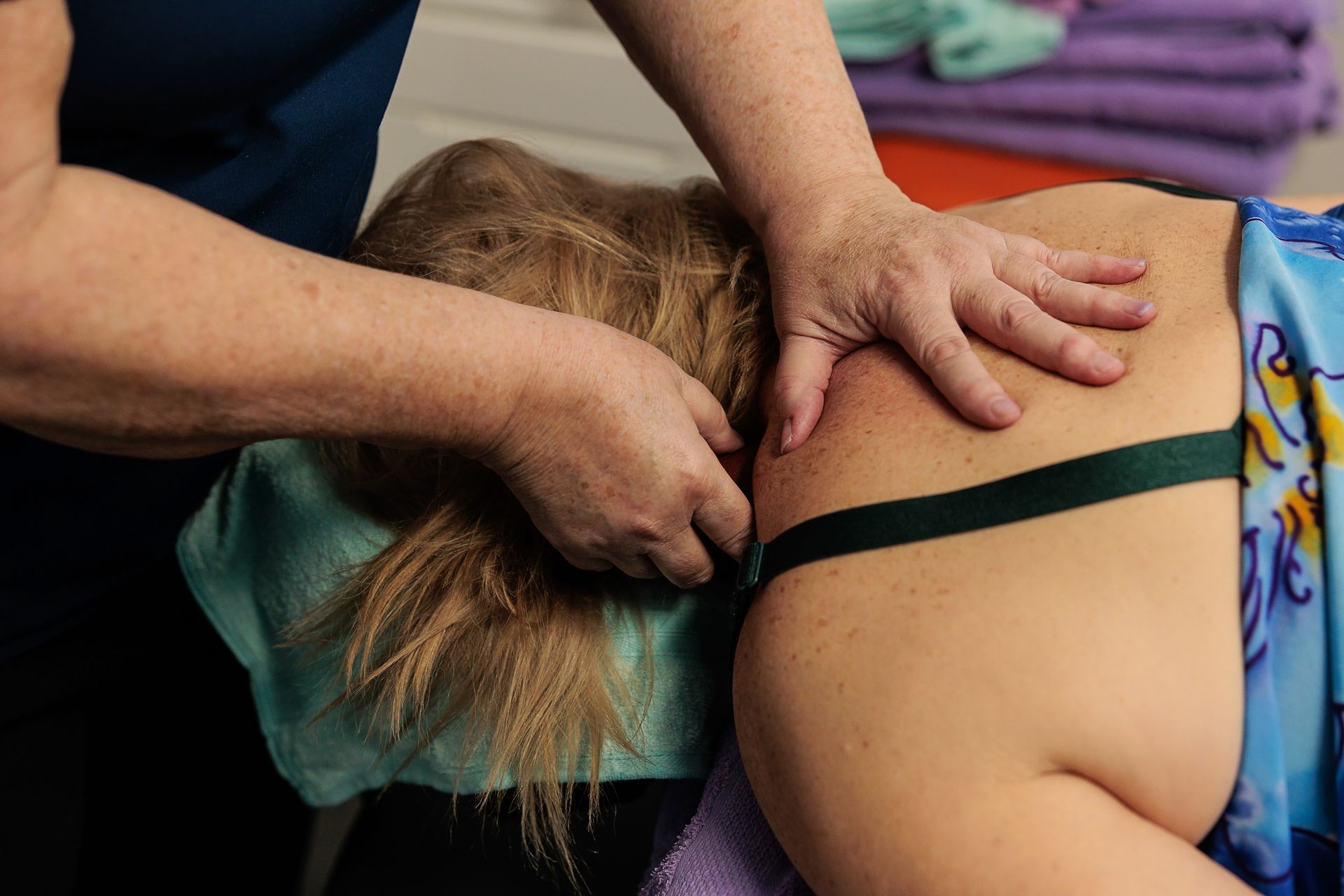 Person receiving a massage; therapist's hands on shoulder and neck. Green strap visible.