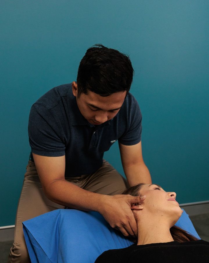 Man Performing Neck Massage on Woman Lying Down. Teal Wall in Background — Grays Chiropractic & Wellness In Walkerston, QLD