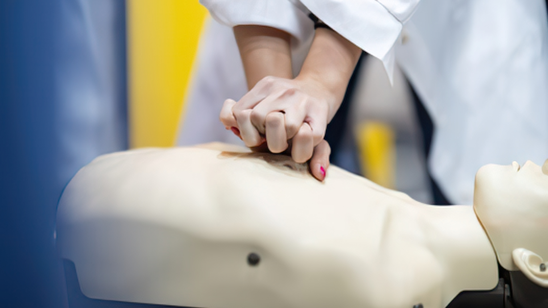 Hands performing CPR chest compressions on a mannequin in a training setting